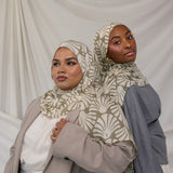 Two women side by side in matching beige and white leaf print hijabs, styled against white background.