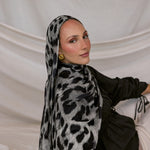 Woman wearing a black and white leopard patterned hijab against a plain background