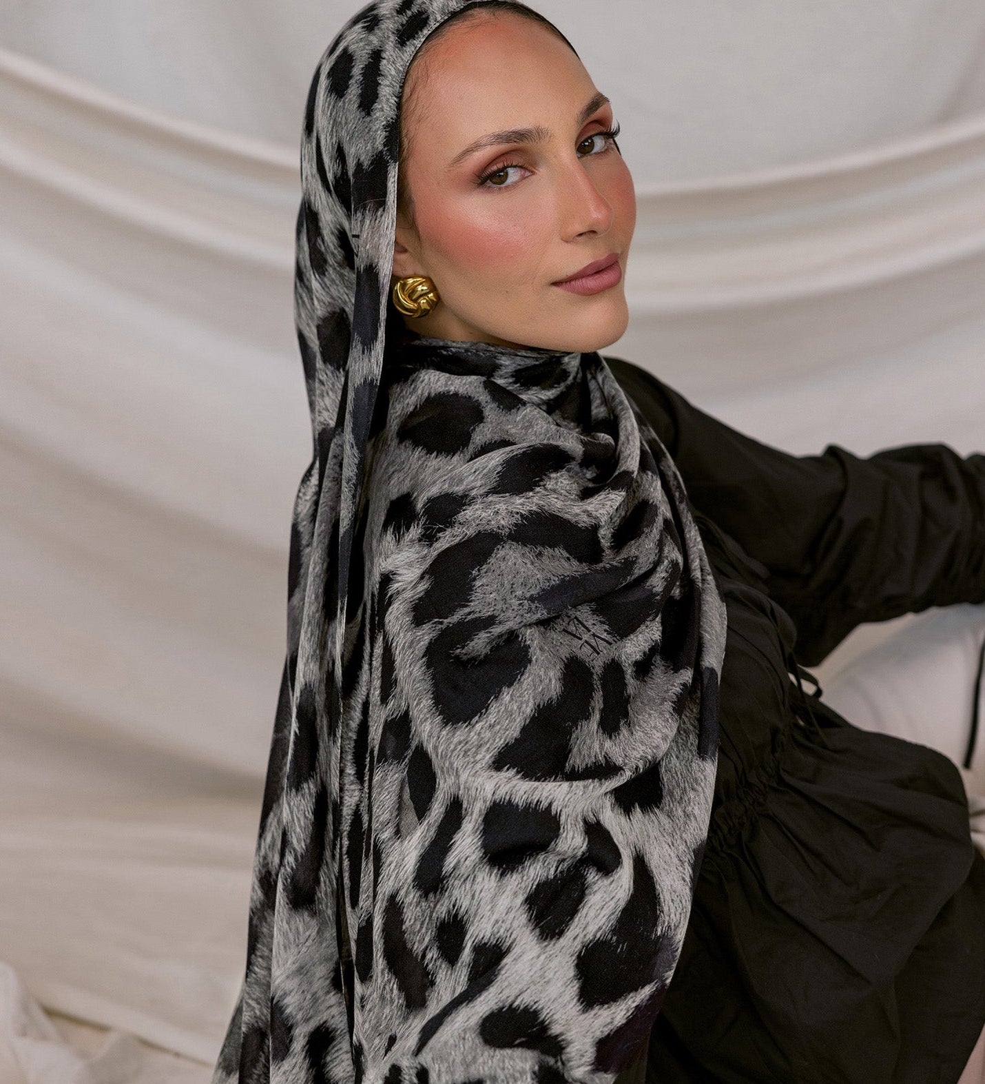Woman wearing a black and white leopard patterned hijab against a plain background