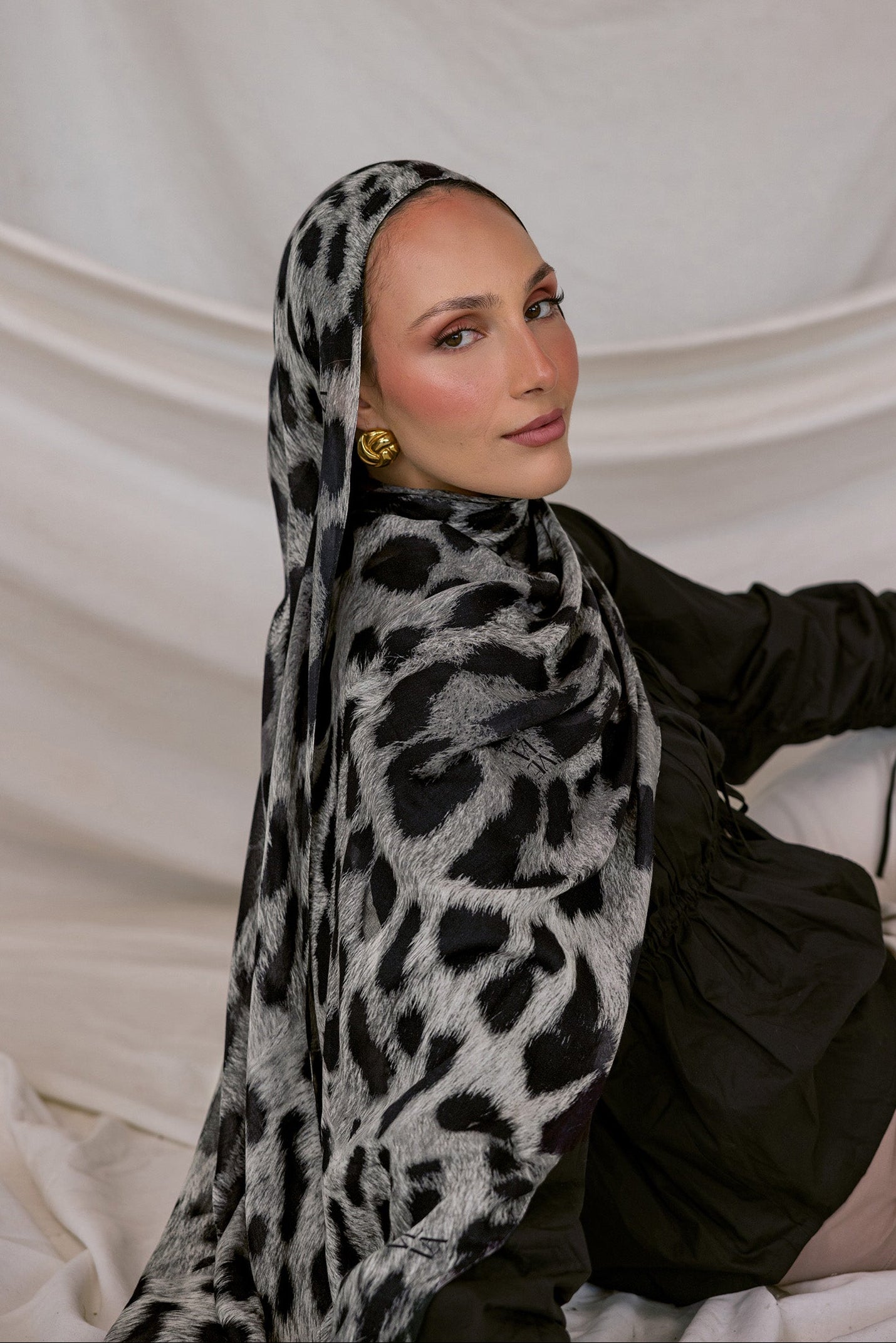 Woman wearing a black and white leopard patterned hijab against a plain background