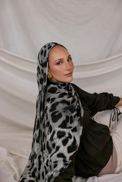 Woman wearing a black and white leopard patterned hijab against a plain background