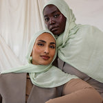 Two women wearing light pastel sea foam green hijabs against a plain background