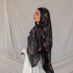 Woman wearing a black pomegranate printed hijab against a plain background