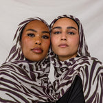 Two models shown wearing VELA's Zebra print, which features a white base and deep berry-toned stripes throughout. 