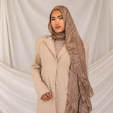 Woman wearing a beige coat and mocha patterned hijab against a plain background