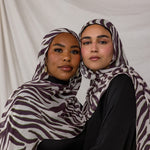 A model shot featuring two models wearing the Zebra print, with a white background on the scarf, overlayed with deep berry toned stripes. 