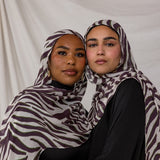 A model shot featuring two models wearing the Zebra print, with a white background on the scarf, overlayed with deep berry toned stripes. 