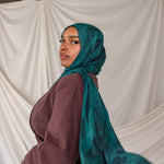 Model wearing a teal peacock inspired printed hijab and brown top against a white backdrop