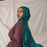 Model wearing a teal peacock inspired printed hijab and brown top against a white backdrop