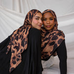 Two models depicted both wearing the Wild Savanna scarf, a peach/tan based scarf with dark spots like an animal, styled in different ways. 