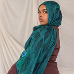 Woman styled in a peacock inspired print hijab with a white draped curtain background