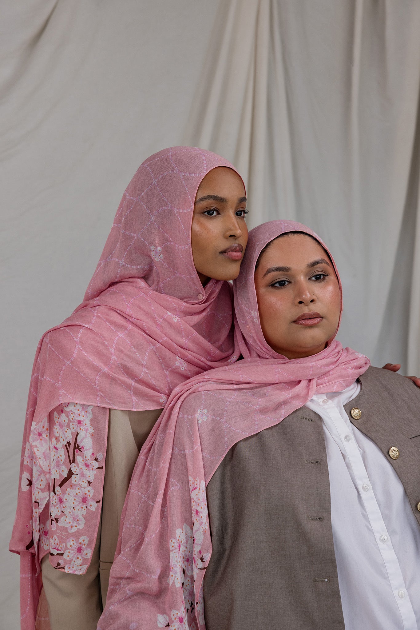 Two models styled in a pink printed hijab featuring cherry blossoms in pink and white. 