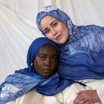 Two women wearing blue with white shell printed hijabs against a white background