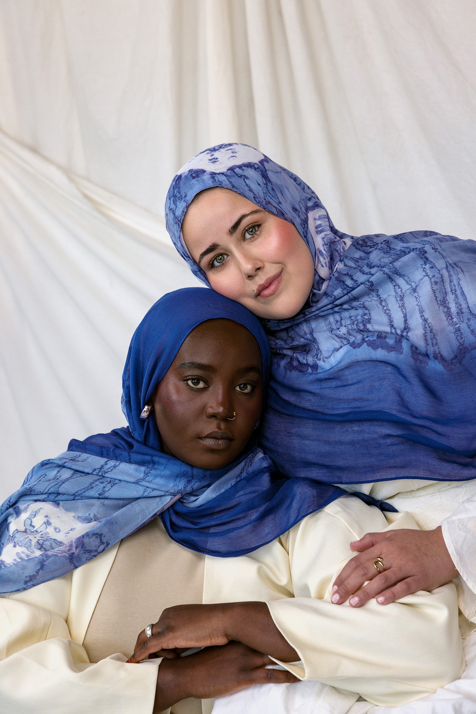 Two women wearing blue with white shell printed hijabs against a white background
