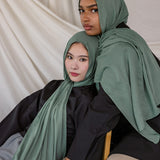 Two women wearing Pine Green hijabs sitting on a white draped background