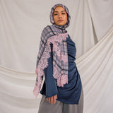 Woman wearing a blue outfit with a pink checkered plaid patterned scarf against a plain background