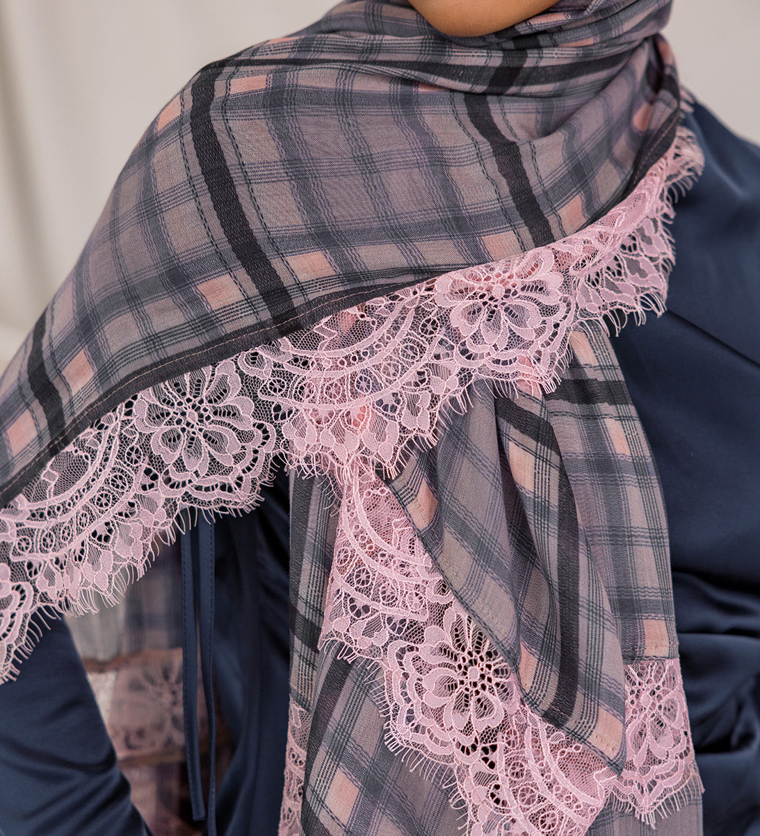 Model styled in a plaid scarf with lace trim over a dark blue outfit.