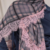 Model styled in a plaid scarf with lace trim over a dark blue outfit.