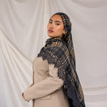 Woman wearing a plaid hijab with lace details over a beige coat against a plain background