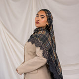 Woman wearing a plaid hijab with lace details over a beige coat against a plain background