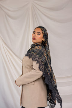 Woman wearing a plaid hijab with lace details over a beige coat against a plain background