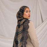 Woman wearing a black orange plaid scarf with lace details on a plain background