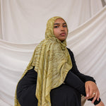 Model wearing a olive printed dune hijab and black outfit against a white draped background