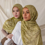 Two women styled in green printed dune hijabs against a plain background.