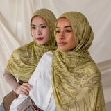 Two women styled in green printed dune hijabs against a plain background.