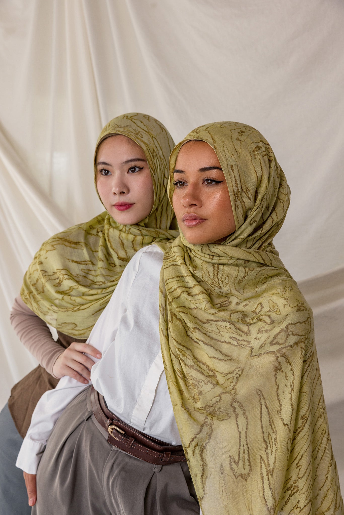 Two women styled in green printed dune hijabs against a plain background.