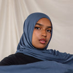 Model wearing a blue hijab against a plain background.