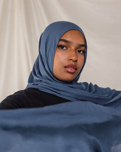 Model wearing a blue hijab against a plain background.
