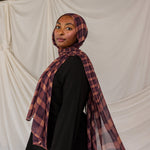 Woman wearing a purple and brown plaid hijab against a plain background