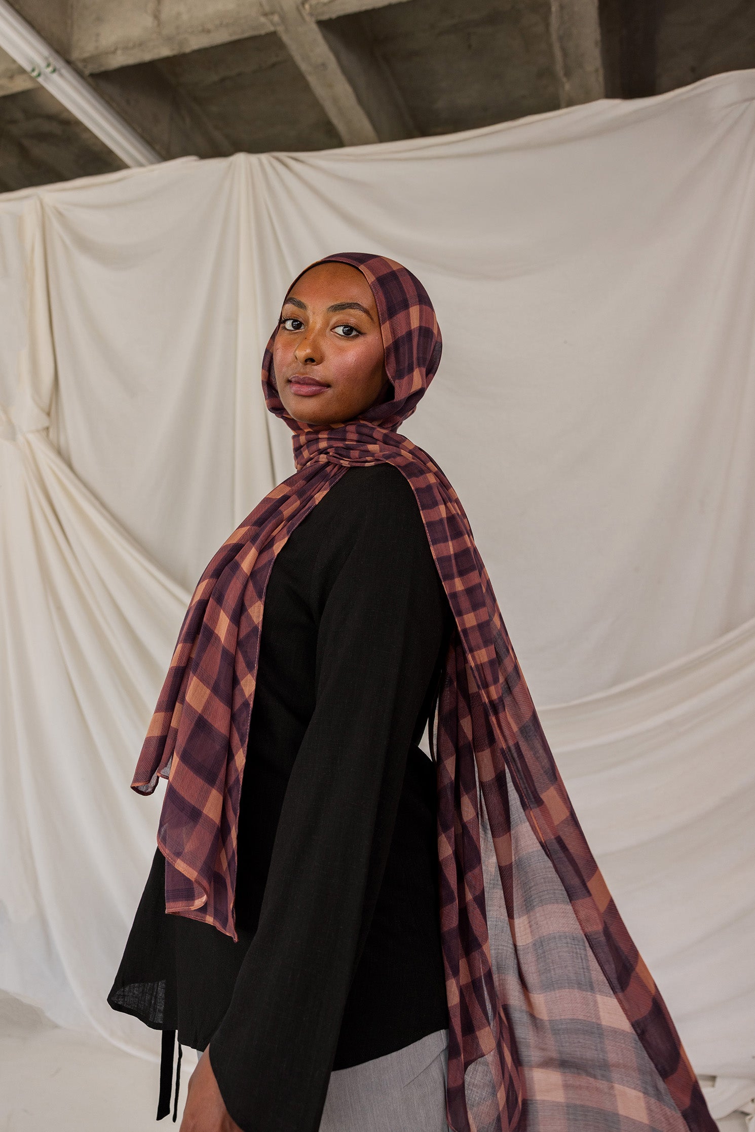 Woman wearing a purple and brown plaid hijab against a plain background