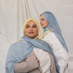 Two women wearing blue / yellow ombre hijabs in front of a plain background