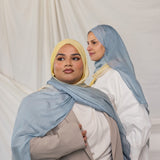 Two women wearing blue / yellow ombre hijabs in front of a plain background