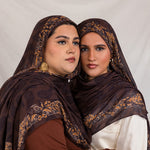 Sister models in Chocolate Paisley hijabs holding each other posed together in studio light.