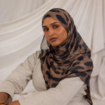 Model styled in a patterned leopard hijab sitting against a white draped background