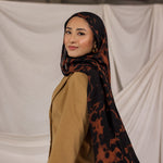 Woman wearing a tortoiseshell patterned hijab and beige top against a plain background