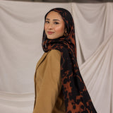 Woman wearing a tortoiseshell patterned hijab and beige top against a plain background