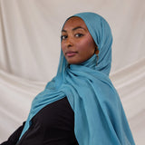 Person wearing a bright blue hijab against a plain background