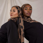 Two women wearing chocolate brown leopard print hijabs against a plain background