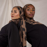 Two women wearing chocolate brown leopard print hijabs against a plain background