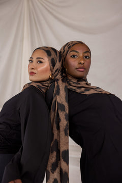 Two women wearing chocolate brown leopard print hijabs against a plain background