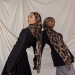 Two women wearing brown leopard print hijabs against a plain background