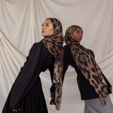 Two women wearing brown leopard print hijabs against a plain background