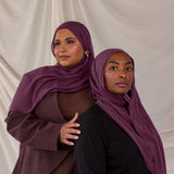 Two models styled in purple red hijabs against a plain background