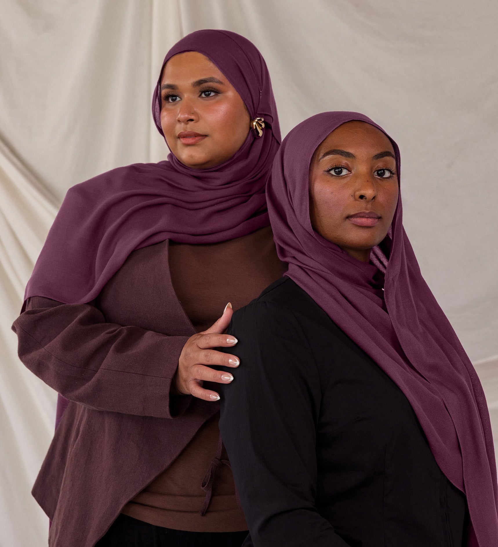 Two models styled in purple red hijabs against a plain background