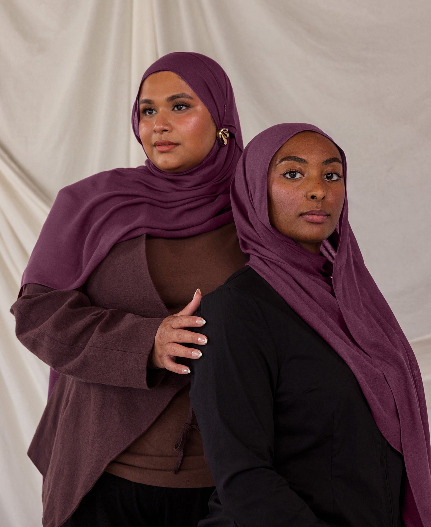 Two models styled in purple red hijabs against a plain background