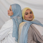 Two girls wearing hijabs in light blue and yellow gradient against a plain background